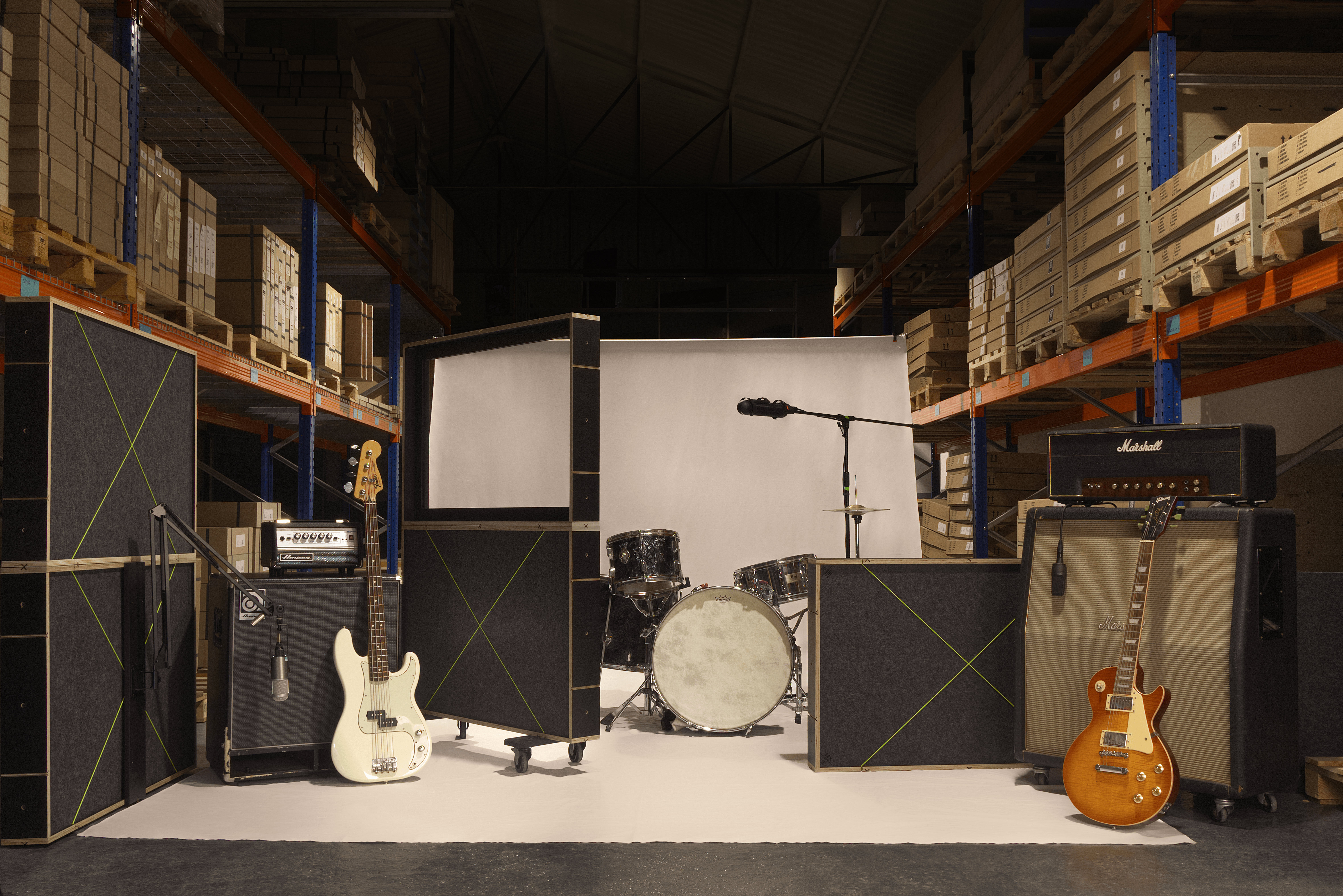 Music equipment including guitars, amplifiers, and a drum set in a warehouse setting.